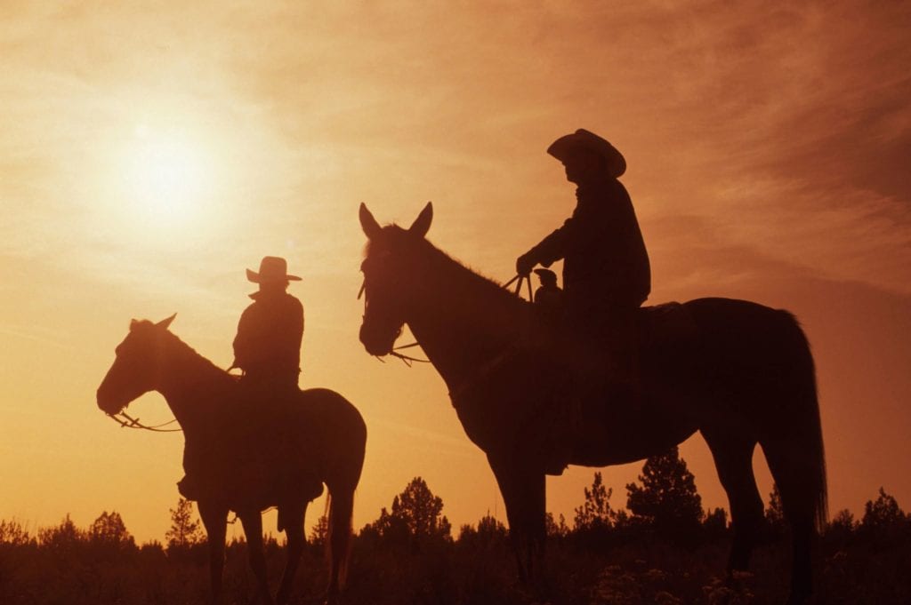 Cowboys riding horses at sunset