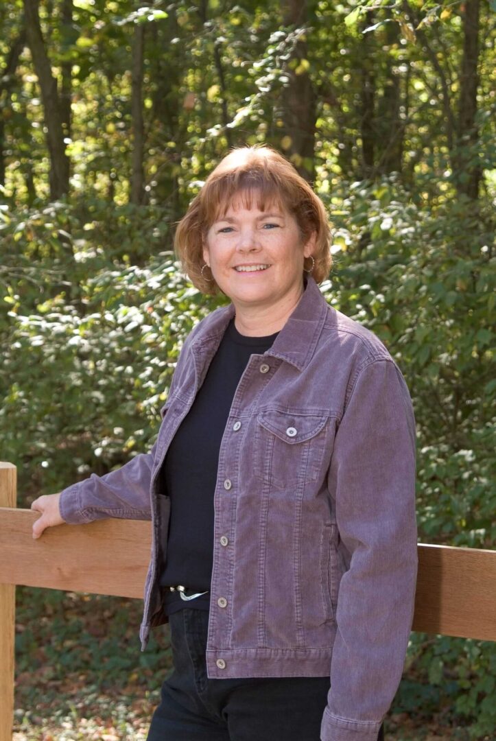 Woman standing beside a wooden fence in front of a forest